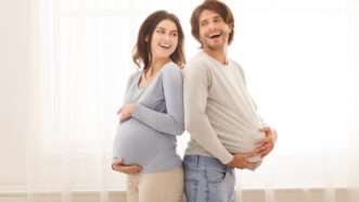 A pregnant woman holds her stomach while a man cradles a fake pregnancy belly. | Prostockstudio | Dreamstime.com