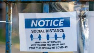 A sign on a fence advising people to social distance and stay six feet apart in order to stop the spread of COVID-19 | Gary Hider | Dreamstime.com